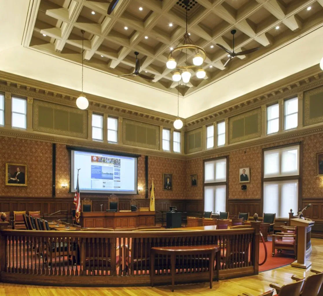 Historic municipal building interior with a high coffered plaster ceiling, ornate plaster cornices and moldings, and plaster-finished walls above wood wainscoting